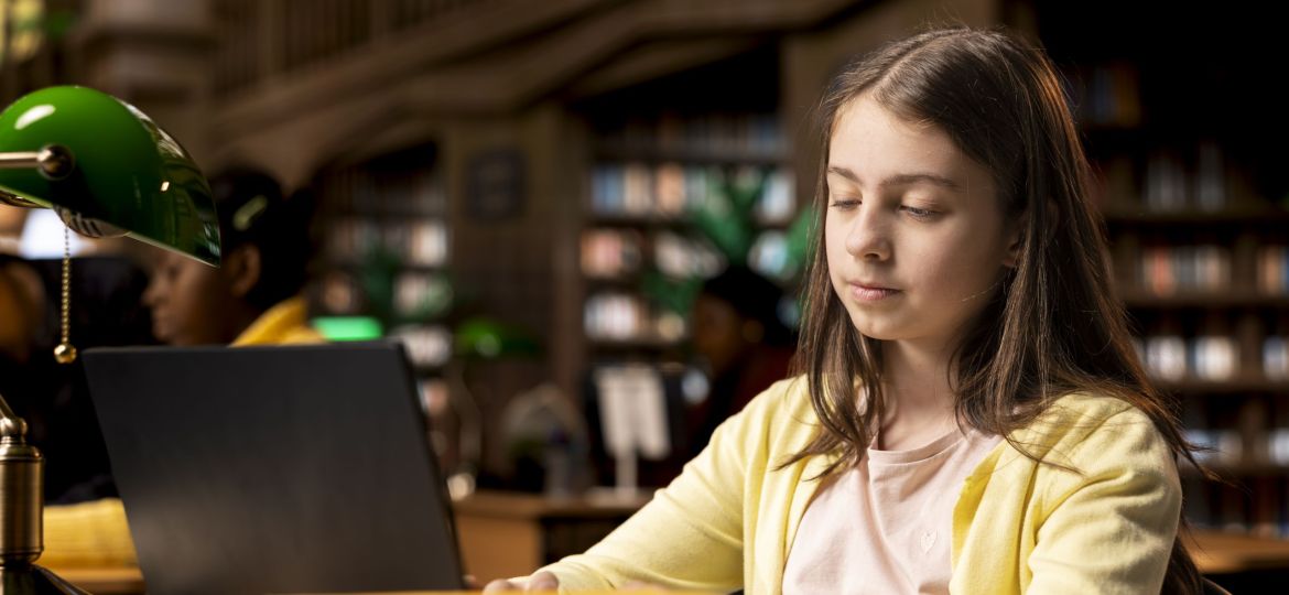 Young student competing her class notes on her laptop during a homework session, working on exercises in the school library. Teenager focusing on modern ways to finish assignments.