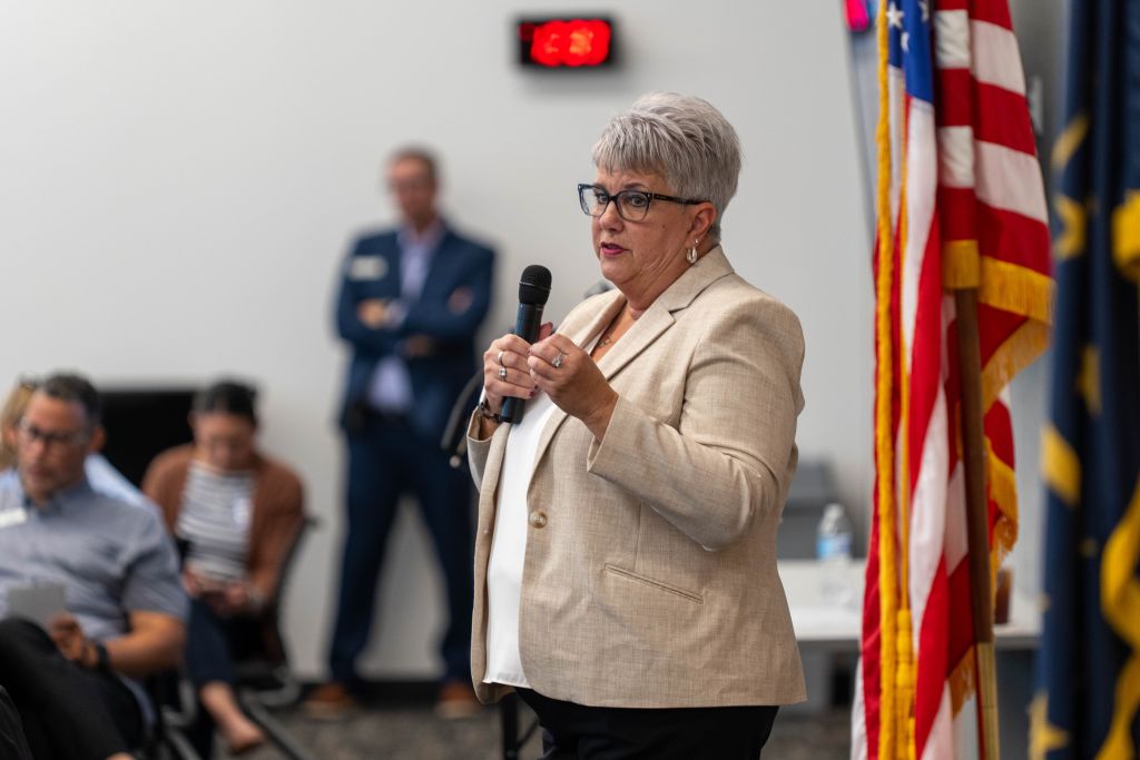Female speaker next to American flag with people in the background.