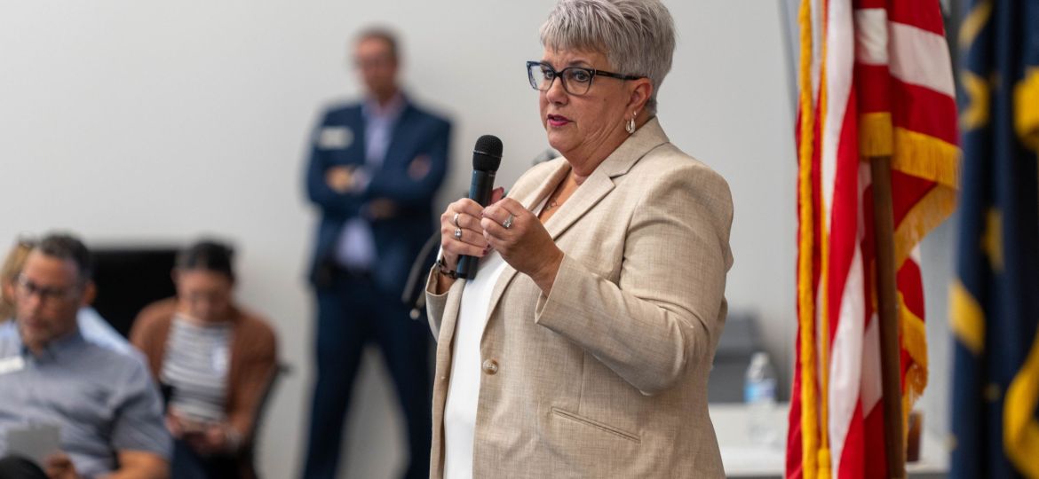 Female speaker next to American flag with people in the background.